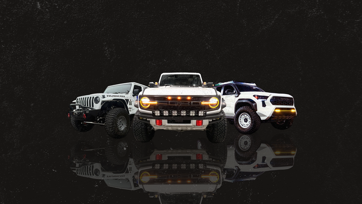 Three off-road vehicles displayed together on a dark reflective studio background: a white Jeep Wrangler on the left, a white Ford Bronco with amber LED light bars in the center, and a white pickup truck on the right.